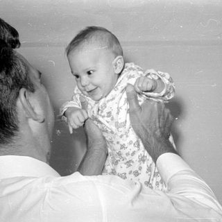 Man holding a baby in a patterned sleeper.