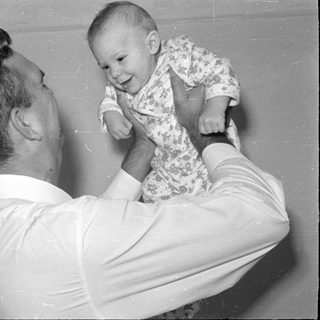 Man holding up a baby in floral sleeper.