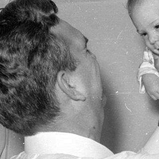 Man holding up a baby in floral sleeper.