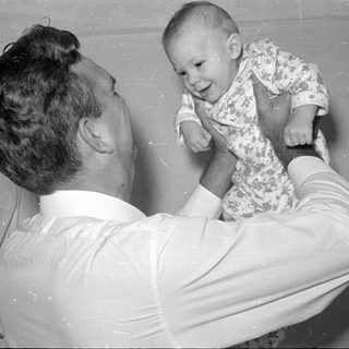 Man holding up a baby in floral sleeper.