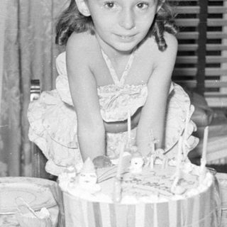 Young girl sitting behind a birthday cake.