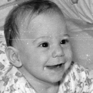 Infant lying in a crib with cartoon wallpaper.