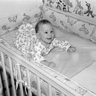 Infant lying in a crib with cartoon wallpaper.