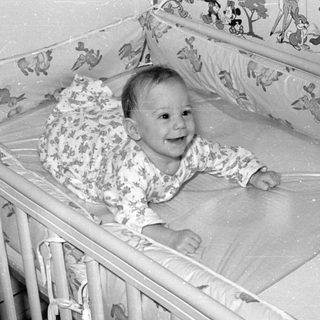 Infant lying in a crib with cartoon wallpaper.