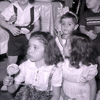 Four children in dress clothes, one holding a lollipop.
