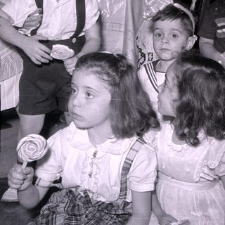 Four children in dress clothes, one holding a lollipop.