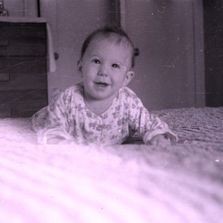 Baby lying on a bed near a wooden dresser.