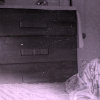 Baby lying on a bed near a wooden dresser.