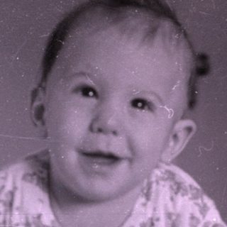 Baby lying on a bed near a wooden dresser.