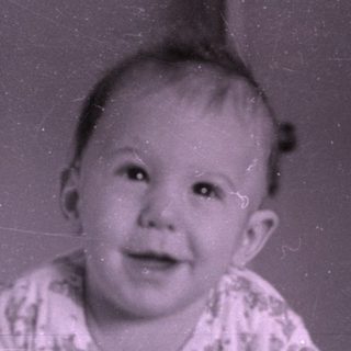 Baby lying on a bed near a wooden dresser.