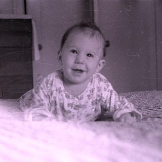 Baby lying on a bed near a wooden dresser.