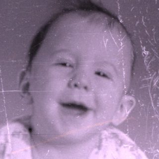 Infant in patterned pajamas lying on a bed.