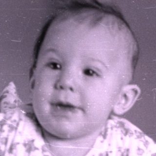 Baby in patterned clothing on a striped blanket.