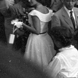 Crowd in formal mid-century attire outdoors.