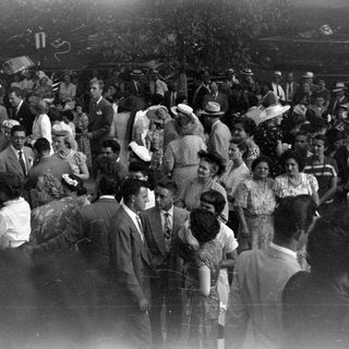 Crowd in formal mid-century attire outdoors.