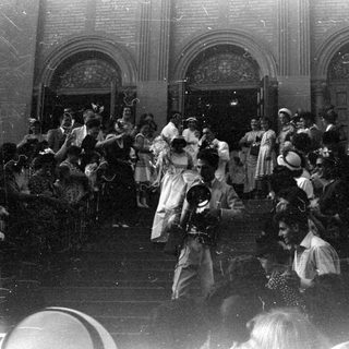 Crowd gathered outside arched doorways with a bride.