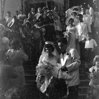 Couple in wedding attire descending stairs with guests.