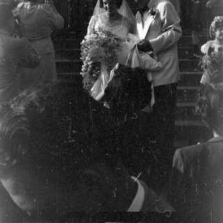Couple in wedding attire descending stairs with guests.