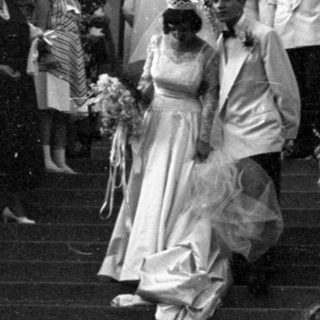 Wedding party descending stone steps of arched building.