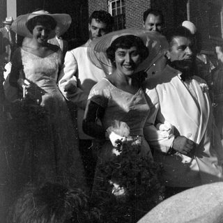 Group in formal white attire by a brick building.