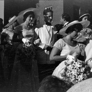 People in formal mid-century attire standing outdoors.