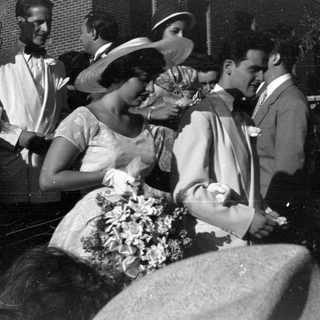 People in formal mid-century attire standing outdoors.