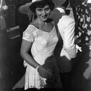 Woman in floral dress and wide hat outdoors.