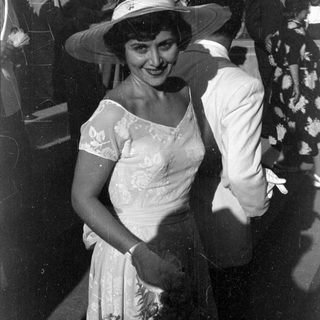 Woman in floral dress and wide hat outdoors.