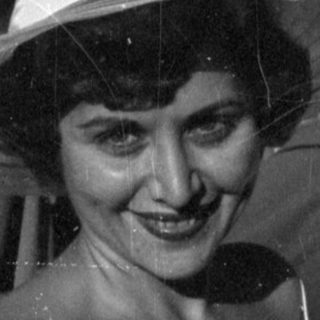 Woman in floral dress and wide hat outdoors.