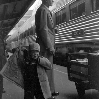 Child and man standing beside a train car.