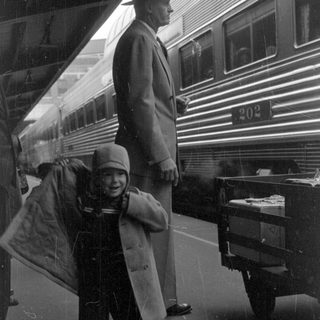 Child and man standing beside a train car.