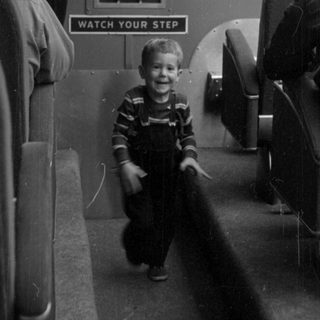 Boy in overalls inside a passenger vehicle.
