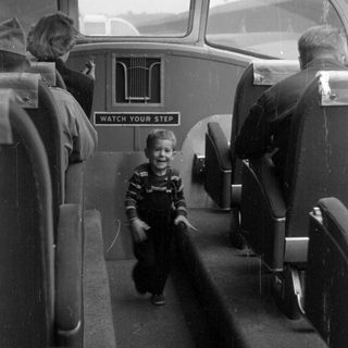 Boy in overalls inside a passenger vehicle.