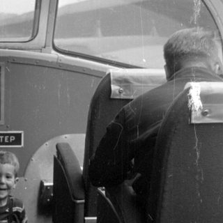 Boy in overalls inside a passenger vehicle.