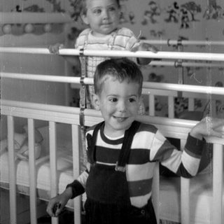 Two children posing by a white crib.