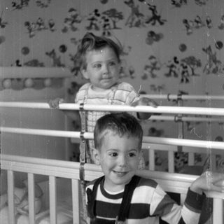 Two children posing by a white crib.