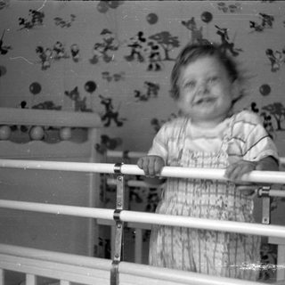 Child in a white crib against patterned wallpaper.
