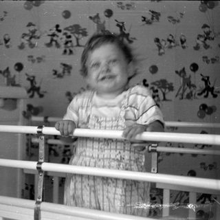 Child in a white crib against patterned wallpaper.