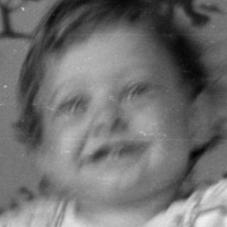 Child in a white crib against patterned wallpaper.