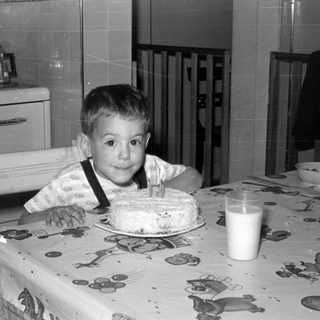 Young boy with birthday cake and milk in kitchen.