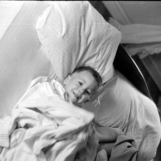 Young child lying in bed under striped blanket.