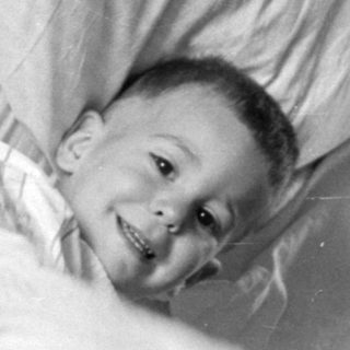 Young child lying in bed under striped blanket.