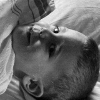Baby lying on a pillow under striped blankets.