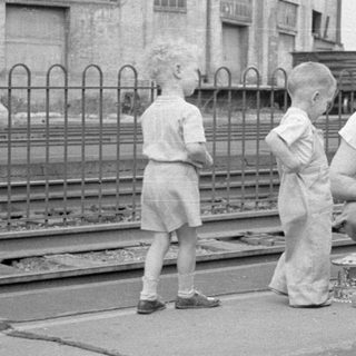 Man and children by railway tracks near industrial building.