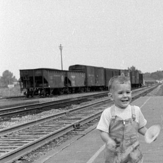 Child in overalls running on a railway platform.
