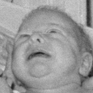 Woman in white uniform with crying infant in bassinet.