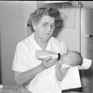 Older woman feeding a baby with a bottle.