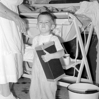 Child in striped overalls holding a box indoors.