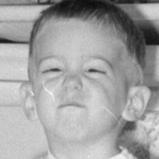 Child in striped overalls holding a box indoors.