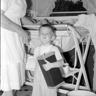 Child in striped overalls holding a box indoors.